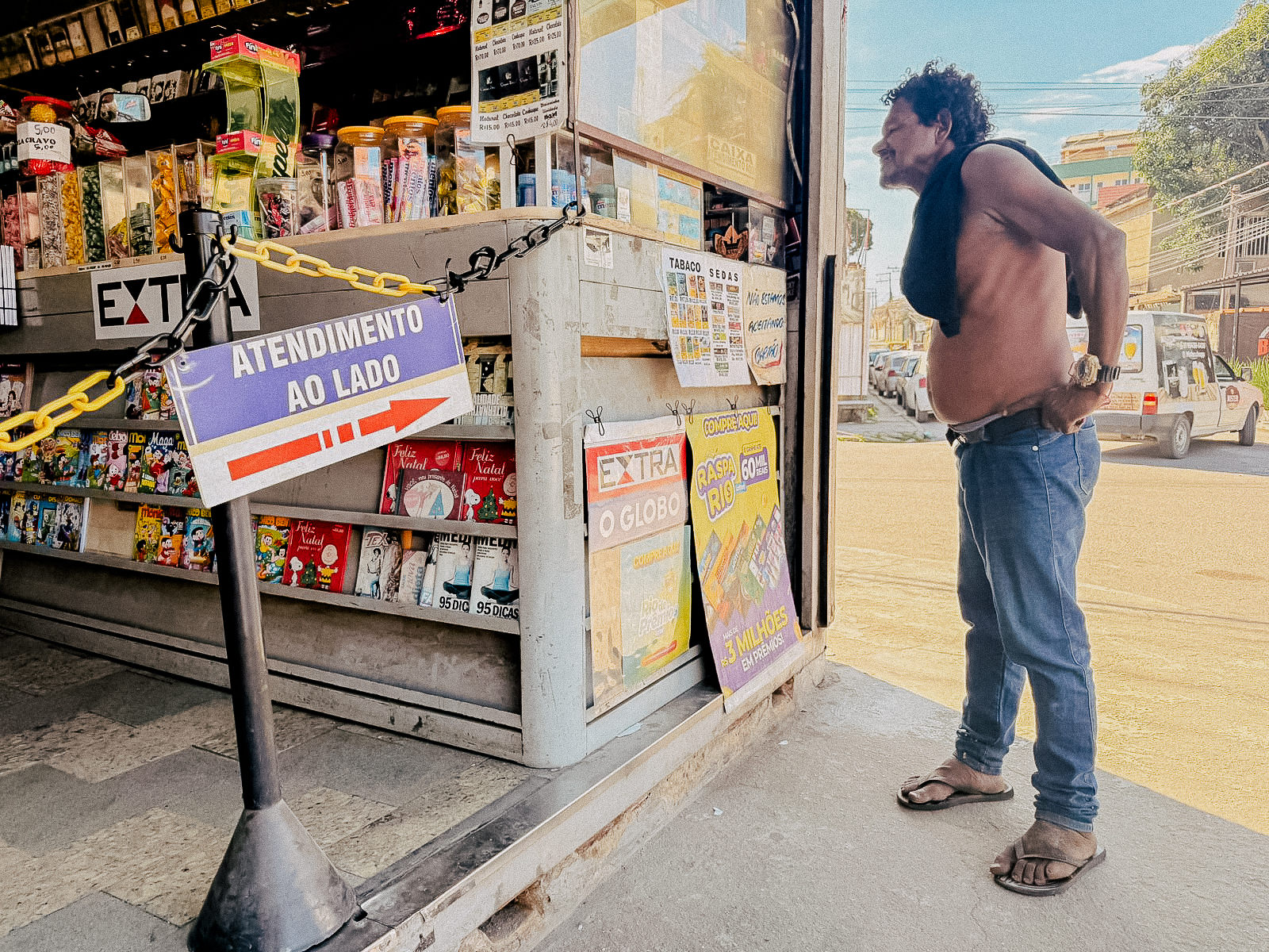 Ele para, observa…as manchetes falam de tudo, menos da vida que acontece ali, na esquina onde a notícia não chega.